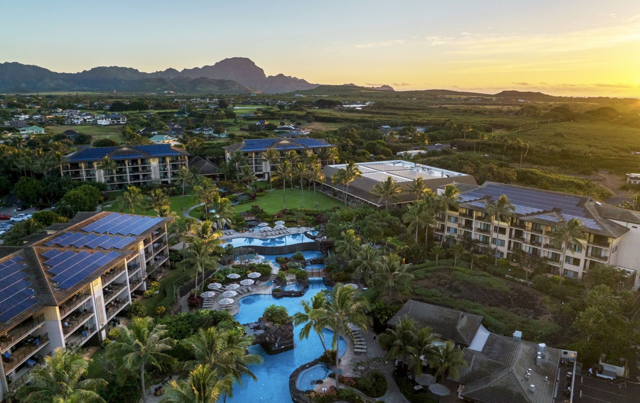 Aerial view of Koloa Landing Resort at sunset, with lagoon pools below and the green mountains of Kauai's south shore behind